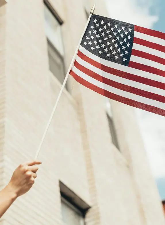 A person holding an american flag in front of a building.